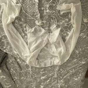 Vit omlott blus från H&M Divided - Säljer en vit, tunn och flowy omlott blus från H&M Divided i storlek S. Blusen har långa ärmar och är gjord i ett lätt, transparent material som ger en luftig känsla. Perfekt att styla med jeans eller kjol för en trendig look.
