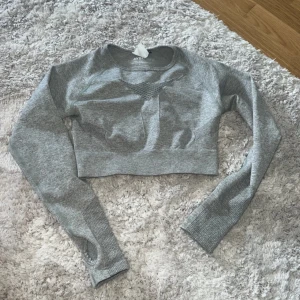 Grå croppad träningströja från AYBL - Säljer en grå croppad långärmad träningströja från AYBL. Tröjan har mesh-detaljer framtill och på ärmarna för extra ventilation, samt tumhål i mudden. Perfekt för gymmet eller sportiga dagar. Materialet är mjukt och stretchigt syntet för maximal komfort.