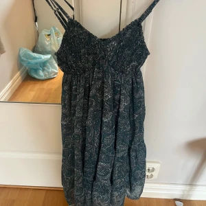 Blå kortklänning från Meet Me There - Supersöt grön kortklänning med smala axelband och snyggt paisleymönster från Meet Me There. Den är aldrig använd och därför i väldigt bra skick, storlek står inte men den passar mig som brukar ha xs/S.