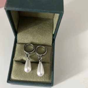 Silverörhängen med droppformad pärla - Snygga örhängen i silverfärg med droppformade vita pärlor som hänger från små ringar. Perfekt för dig som gillar stilrena detaljer med lite extra glans. Passar till både casual och mer uppklädda looks. 