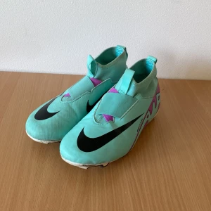 Nike Mercurial Air Zoom fotbollsskor - Säljer ett par Nike Mercurial Air Zoom fotbollsskor i en fräsch turkos färg med lila och svarta detaljer. Skorna har en strömlinjeformad design, låg profil och kardborreband över vristen. Yttermaterialet är syntet och sulan har dobbar för gräsplan. Perfekt för dig som vill sticka ut på planen. Jag har änvänt dom i cirka 1 år storlek 38 pris kan diskuteras 