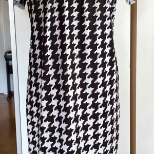Svartvit rutig kortklänning Laura Kent - Snygg kortklänning från Laura Kent i storlek 36 med klassiskt svartvitt rutigt mönster. Klänningen har korta ärmar och rak passform, perfekt för dig som gillar grafiska prints och vill sticka ut. Materialet är mjukt och följsamt, vilket gör den bekväm att bära hela dagen.
