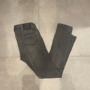 Grå slim jeans Jack & Jones Glenn - Snygga grå jeans från Jack & Jones i modellen JJGLENN JJORIGINAL SQ 650 och storlek 29/32. Jeansen har en slim passform, klassisk femficksdesign och diskreta sömmar på bakfickorna. Perfekta för dig som gillar en smal siluett och stilren look. Sriv för ytterligare bilder