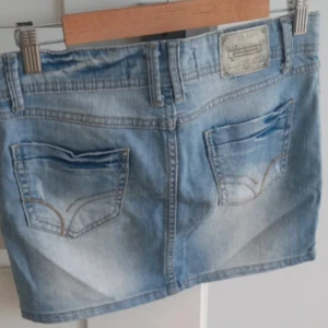 Blå jeanskjol med fickor, strl 36 - Snygg ljusblå jeanskjol i klassisk femficksmodell med slitningar och detaljerade sömmar. Kjolen har knapp och dragkedja framtill samt bälteshällor. Passar dig som gillar en chill och avslappnad stil.