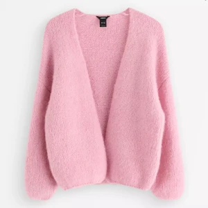 Ljusrosa stickad kofta från Lindex - Supermjuk och fluffig ljusrosa stickad kofta från Lindex. Koftan har en öppen front utan knappar, långärmade ärmar och en oversized, cozy passform. Perfekt att slänga på sig när du vill vara både chill och snygg. Materialet är stickat och känns riktigt gosigt. Oanvänd!