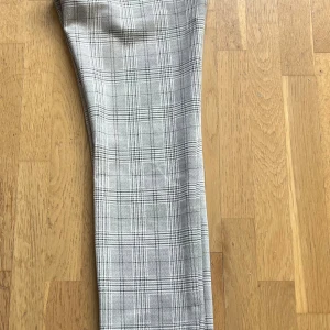 Grå rutiga kostymbyxor Parami - Snygga grå kostymbyxor från Parami med klassiskt rutigt mönster. Byxorna har raka ben och bälteshällor, perfekta för en clean och stilren look. Materialet känns mjukt och har en lätt struktur. Använda en gång och dyra i inköp (1000kr+)