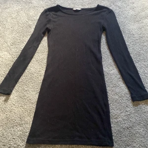 Svart ribbad långärmad klänning  - Snygg svart ribbad klänning i storlek 158/164. Modellen är figurnära med lång ärm och rund halsringning. Perfekt för dig som gillar enkel och stilren design med en touch av edge. Passar dig som vill ha en klassisk look med modern känsla.