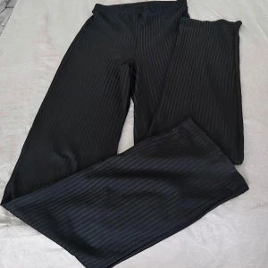 Svarta ribbade byxor från NLYONE - Säljer ett par svarta byxor från NLYONE i storlek S. Byxorna har ett snyggt diskret ribbat mönster och är raka i modellen. Perfekta för dig som gillar en stilren look med lite edge.