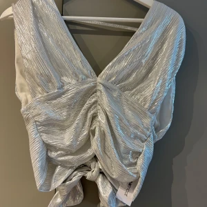 Silver topp med knyt från Gina Tricot - Så fin glittrig silveig topp från Gina Tricot med djup v-ringning och snygg knytning i ryggen. Storlek S. Aldrig använda, med prislapp kvar. Mitt pris 200 kr. Köparen står för frakten🫶🏻