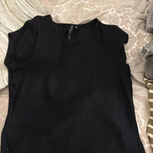 Svart ribbad topp från lager 157 - En svart ribbad topp från lager 157 med rund halsringning och korta ärmar. Enkel och stilren modell som passar perfekt till jeans eller kjol. Mjuk och stretchig för en bekväm känsla.