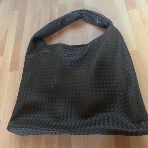 Brun flätad axelväska i skinnimitation - Säljer en stor brun axelväska med flätad design. Väskan har en bred axelrem och är tillverkad i skinnimitation. Perfekt för dig som gillar en stilren och trendig look med plats för allt du behöver. använd endas 1 gång