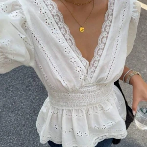 Vit blus med spets och puffärm - Superfin vit blus med broderade detaljer och spetskantad v-ringning. Blusen har puffiga korta ärmar, smockad midja och volang nertill. Perfekt för dig som gillar romantisk och feminin stil. Tillverkad i bomull för en luftig känsla.