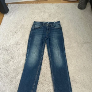 Blå jeans 2X REX Regular strl 146 - Snygga blå jeans från 2X REX i regular fit, storlek 146. Klassisk femficksmodell med dragkedja och knapp, i slitstark denim med lätt tvättade detaljer. Perfekta för en avslappnad och cool vardagsstil.