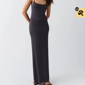 Svart lång slipklänning med smala axelband - Säljer en svart lång slipklänning med smala axelband och figurnära passform. Klänningen har en stilren och minimalistisk design som ger en snygg siluett. Perfekt för dig som gillar enkla och eleganta plagg med lite edge.