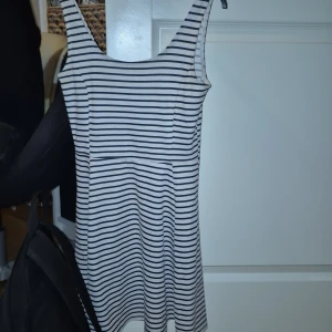 Randig kortklänning från H&M Divided - Säljer en vit och marinblå randig kortklänning från H&M Divided i storlek 36. Klänningen är ärmlös med rundad hals och har en lätt utställd passform. Perfekt för sommarens alla dagar, till sneakers eller sandaler. Materialet är mjukt och skönt bomull.