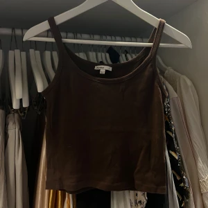 Brunt kort linne - Säljer en brun croppad linnetopp från Subdued med smala axelband och rund halsringning. Toppen är enkel och stilren, perfekt att matcha med jeans eller kjol. Väldigt mjuk bomullskänsla och snygg passform som sitter tajt men bekvämt.