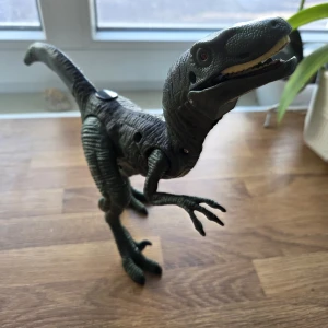 Dinosaurie som kan ryta - Bilderna visar en leksaksdinosaurie, troligen en velociraptor, med rörliga leder och lysande ögon. Den är grön med detaljerad struktur och passar perfekt för dig som gillar dinosaurier och äventyr. Perfekt för unga dinosauriefans och samlare! Dinosaurien kan ryta! Sparsamt använd, fint skick. 