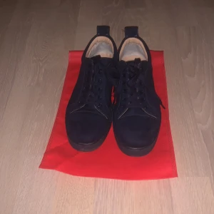 Christian Louboutin mörk blå sneakers - Säljer ett par mörka blå sneakers från Christian Louboutin med ikonisk röd sula. Skorna har snörning och är tillverkade i skinn. Kommer med originalkartong och dustbags. Perfekta för dig som vill sticka ut med en lyxig och klassisk streetstil. Kom med minsta frågorna. Sista bild så kan man fixa kostar ba 200kr på en skomakare