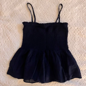 Marinblå linnetopp med volang - Supersöt marinblå linnetopp som går att ha som tubtopp, med smockad överdel och tunna axelband. Toppen har en volangig nederdel som ger en luftig och somrig känsla. Perfekt till jeans eller kjol. Helt ny i storlek 170 men sitter som S/M