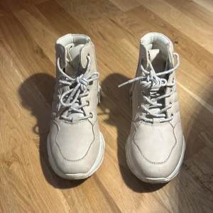 Beige chunky boots med snörning - Beiga skor med högt skaft, snörning framtill och dragkedja på sidan. Skorna har en kraftig platt sula Perfekta för dig som gillar streetstyle och vill sticka ut. Skorna har tappat lite färg på sidorna men det är inget man tänker på så därför skulle jag säga att skorna är i bra skick!