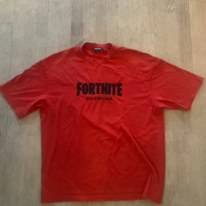 Röd Fortnite x Balenciaga t-shirt - Limited edition röd t-shirt från Balenciaga i samarbete med Fortnite. Stor svart print på bröstet med båda loggorna. Klassisk rund hals och korta ärmar. Tillverkad i mjuk bomull för skön känsla och loose passform. Perfekt för dig som gillar gaming och streetwear. Älskar verkligen tishan men vill bli av med den för vintern. Så va inte rädd att fråga något eller skicka bud ;). Skick 9,5/10