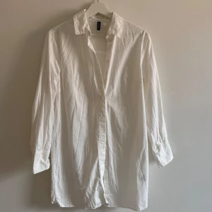 Vit långärmad skjorta från H&M Divided - Klassisk vit skjortklänning från H&M Divided i bomull. Skjortan har lång ärm, knappar framtill och vid manschetten samt en rak passform. Perfekt att styla oversized eller som lager-på-lager. Enkel och stilren design som funkar till många looks. Varsamt använd, ser inga skavanker. Jag har massor av artiklar till salu! Köp flera och få rabatt!