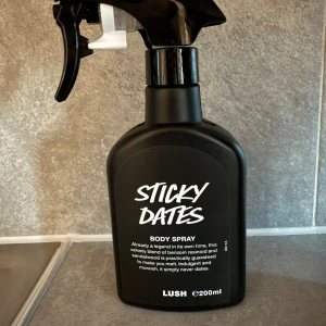 Sticky Dates Body Spray från Lush ny! - Sticky Dates Body Spray från Lush i en svart plastflaska med spraymunstycke. Doften är en mix av benzoin och sandelträ, vilket ger en söt och varm känsla. Flaskan rymmer 200 ml och har en modern, stilren design med vit text på svart bakgrund.helt ny!:)