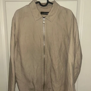 Beige overshirt från J.Lindeberg - Stilren beige overshirt från J.Lindeberg med klassisk krage och hel dragkedja framtill. Jackan är tillverkad i ett lätt linnematerial och har en avslappnad passform. 