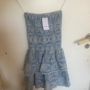 Blå broderad kortklänning Subdued - NYPRIS: 678KR                                                             Supersöt blå kortklänning från Subdued med vitt broderat mönster och volangdetaljer. Klänningen har smockad överdel, tunna axelband och två lager med vågiga kanter. Perfekt för sommarens alla tillfällen, riktigt skön och luftig i bomull.