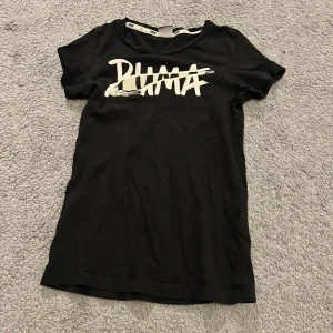 Svart Puma t-shirt med tryck - Svart t-shirt från Puma med coolt vitt logotryck över bröstet. Klassisk rund hals och korta ärmar. Mjuk och skön bomull som passar perfekt till jeans eller shorts. 