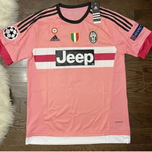 Juventus Pogba rosa matchtröja Adidas - Juventus fotbollströja i rosa med Pogba och nummer 10 på ryggen. Adidas-märke, Jeep-logga på bröstet och svarta ränder på axlarna. Kortärmad med svarta och röda detaljer, tillverkad i lätt och ventilerande climacool-material. Perfekt för dig som älskar fotboll och Juventus.