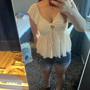 Vit volangblus med knyt från 157 - Supersöt vit blus från 157 med volangärmar och v-ringning. Toppen har knyt framtill och en flowy, luftig passform. Använd men i bra skick.