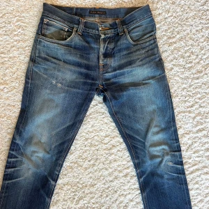 Grim Tim Selvedge Nudie Jeans Co - Ett par blåa selvedge jeans i 100% bomull från nudie jeans. Byxorna är köpta i deras butik i Göteborg. Förutom de synliga slitningarna så har ena framfickan ett hål. Om övriga frågor uppstår så kontakta mig!
