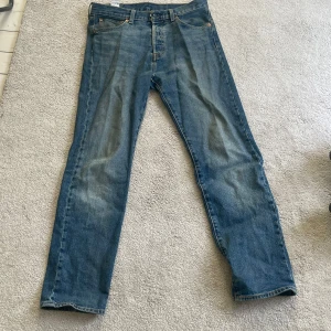 Levi's 501 blå jeans straight fit - Klassiska blå Levi's 501 jeans med rak passform och normal midja. Jeansen är i denim med snyggt sliten tvätt och har fem fickor samt knappgylf. Perfekta för dig som gillar tidlös stil och vill ha ett par ikoniska jeans i garderoben.