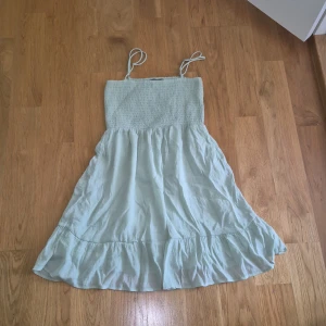 Ljusgrön kort klänning från FB Sister - Supersöt ljusgrön klänning från FB Sister i storlek M. Klänningen har smockad överdel, justerbara smala axelband och volangkant nedtill. Den är lätt och luftig, perfekt för varma dagar. Materialet känns mjukt och har en skön bomullskänsla.