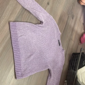 Ljuslila stickad tröja FB Sister - Supermysig ljuslila stickad tröja från FB Sister i ribbad modell. Tröjan har rund hals, långa ärmar och breda muddar vid ärmslut och nederkant. Perfekt att slänga på sig när det är lite kyligt ute. Passar dig som gillar en chill och enkel stil.