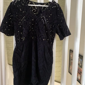 Svart kort spetsklänning Bik Bok - Supersnygg svart kort klänning från Bik Bok med broderad spets och coola hålmönster. Klänningen har korta ärmar, V formad hals, inbyggda shorts och dekorativa tygklädda knappar framtill. Perfekt för dig som gillar detaljer och vill sticka ut lite extra. Pris kan förhandlas.