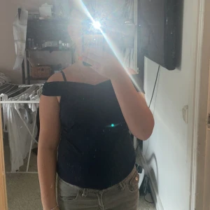 Mörkblå offshoulder topp - Säljer en mörkblå offshoulder topp med smala axelband och snygg twistad detalj framtill. Toppen har en figurnära passform och är perfekt för dig som vill ha en stilren men ändå trendig look. Passar till både jeans och kjol för en cool vibe.