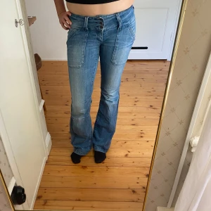 Blå bootcut jeans från only  - Säljer ett par ljusblå bootcut jeans med snygga detaljer som dubbla knappar i midjan, stora framfickor och dragkedjor på bakfickorna. Jeansen har låg midja och är tillverkade i klassiskt denimtyg. Perfekta för dig som gillar en retro vibe.