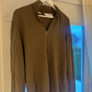 Half zip tröja från Selected Homme - Säljer en brun långärmad tröja från Selected Homme i storlek XL. Tröjan har en stilren half zip-dragkedja vid halsen och är gjord i mjuk bomull. Perfekt för dig som gillar enkel och clean stil med lite edge.