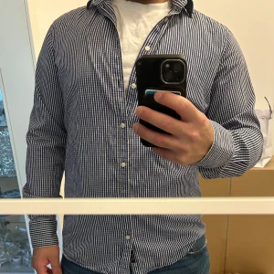 Randig skjorta  - Snygg skjorta i blått och vitt med smala  ränder. Skjortan är i ett mjukt bomullstyg som känns skönt mot huden. Storlek 40 sitter som M/L