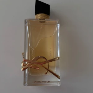 Yves Saint Laurent Libre Eau de Parfum - Säljer en ikonisk parfym från Yves Saint Laurent – Libre Eau de Parfum. Flaskan är rektangulär i genomskinligt glas med guldig detalj och svart asymmetrisk kork. Doften är lyxig och flaskan har en modern design med YSL-logga i metall. Perfekt för dig som gillar eleganta och trendiga parfymer.