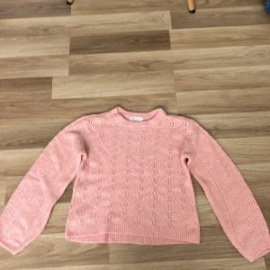 Rosa stickad tröja  - Säljer en söt ljusrosa stickad tröja från H&M i storlek 146/152. Tröjan har ett fint hålmönster och ribbade muddar vid ärmslut och nederkant och vid halsen. Tröjan är jättefin och skön!