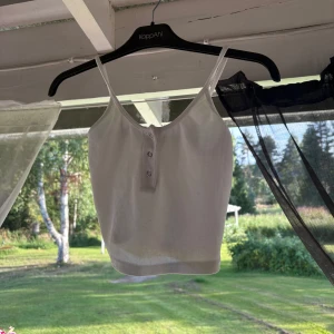 Vit ribbad linnetopp med knappar - Vit croppad linnetopp med smala axelband och ribbad struktur. Toppen har tre små knappar framtill för en enkel men snygg detalj. Perfekt för varma dagar och enkel att matcha med jeans eller kjol. Se sista bilden där det finns en defekt där man ser hålet!🥰❤️