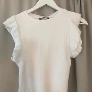 Vit Topp - Säljer en vit volang topp från zara som är helt oanvänd med prislappen kvar. Säljer den för att den ej kommer till användning tyvärr. 