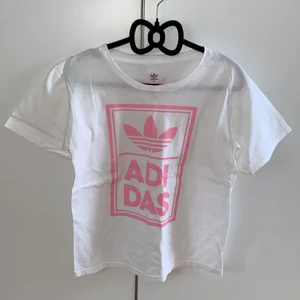 Addidas tshirt vit med rosa tryck - En vit addidas tshirt med rosa tryck. Ett stort tryck på framsidan och ett litet på baksidan. Bara använd en gång. Inte stor i storleken 