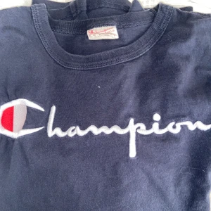 Champion t-shirt  - Säljer en super fin marinblå t-shirt från champion, texten är sydd och är alltså inte ett tryck som de är på deras senaste tröjor. Den är i bomull men är lite tjockare i matrialet och är i väldigt bra skick. Vid fler frågor eller bilder skriv privat😊 Priset kan diskuteras.
