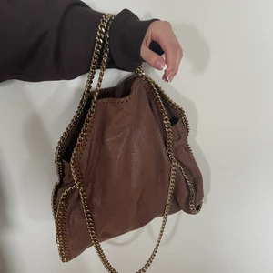 Stella McCartney  - Säljer min Stella McCartney väska i rostbrun! Nypris 9 140 kr säljer för 4 500 kr. Den är i en ovanlig färg och i fint skick! Handtagen är det enda som är lite slitet då den guldiga färgen bleknat lite. Köpt på Vestiaire collective så finns intyg på äkthet. Dustbag medföljer, kan mötas upp i Göteborg eller fraktas. Mått: 34 b x 37 h x 9 d. Har tre guld kedjor. 