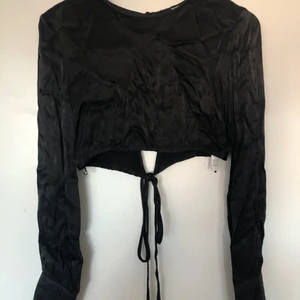 Svart satintopp - Svart satintopp i croppad modell från Bershka. Sitter så fint på men kan tyvärr inte använda den då den är lite för liten på mig. 