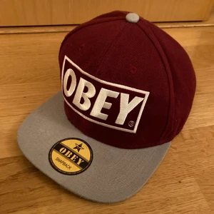 Obey gray red snap back baseball cap - An Obey dark red and gray snap back baseball cap with the golden sticker still on. Gotten as a gift. Good condition.